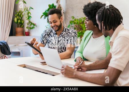 Eine vielfältige Gruppe von Fachleuten arbeitet in einem hellen, anlagenreichen Co-Working-Bereich zusammen, tauschen Ideen aus und nutzen digitale Geräte Stockfoto