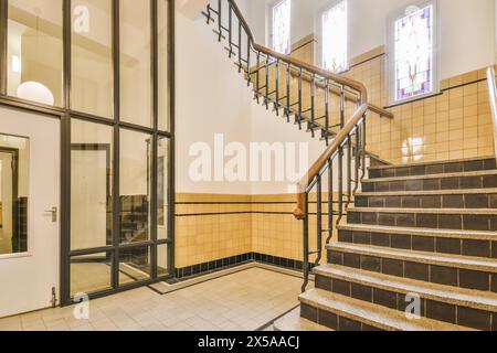 Helles und luftiges Treppenhaus mit klassischem Treppenhaus mit Fliesendetails, großen Fenstern und farbenfrohen Buntglasakzenten. Stockfoto