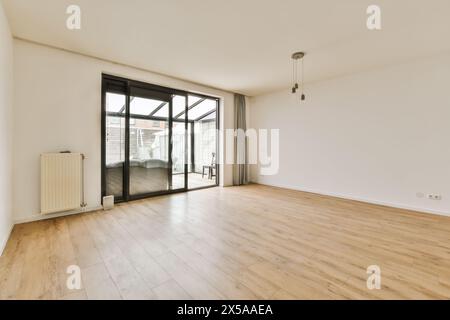 Geräumiges und helles leeres Wohnzimmer mit Hartholzfußboden, riesiger Glasschiebetür, die zu einer Außenterrasse führt, und minimalistischer Pendelleuchte Stockfoto