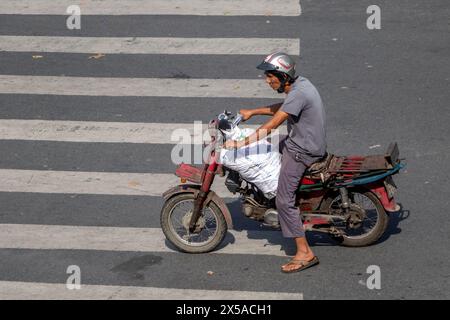 SAIGON, VIETNAM, 17. Dezember 2017, Ein Mann mit einem Motorrad, beladen mit einer Tasche, steht an der Kreuzung Stockfoto