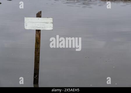 Kleines weißes, verwittertes, leeres hölzernes Schild an einem Pfosten in einem ruhigen, ruhigen Pool von Wasser. Stockfoto