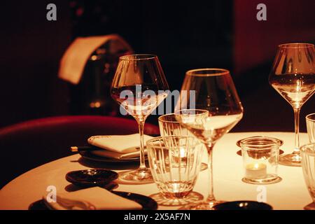 Serviert werden Tische mit weißen Tischdecken mit Tellern, Gläsern und weißen Servietten in einem luxuriösen Restaurant im Dunkeln Abend. Leere Sitze auf einem Tisch. Stockfoto