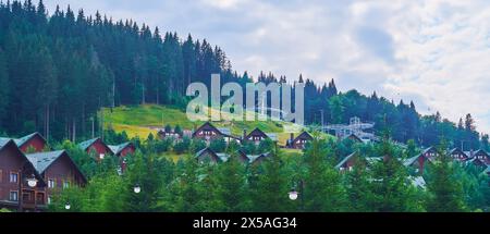 Panorama der hölzernen Bungalows am Berghang in der Umgebung der hohen Nadelwälder der Karpaten, Bukovel, Ukraine Stockfoto