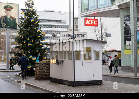 Berlin, Deutschland - 16. Dezember 2023: Checkpoint charlie mit weihnachtsbaum mit ukrainischen Fahnen. Foto des russischen Soldaten und der Menschen, die auf der Straße sichtbar sind. Stockfoto