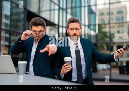 Ausdrucksgesicht eines emotionalen Geschäftsmannes. Ein seriöser Geschäftsmann, der mit dem Finger auf Sie zeigt. Porträt eines Geschäftsmannes im Anzug im Freien. Das zwei Business-Team Stockfoto