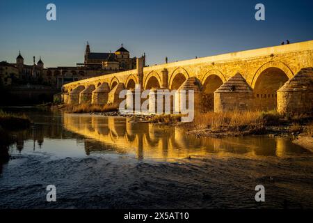 Die römische Brücke von Cordoba ist in goldenes Licht getaucht und reflektiert den Fluss Guadalquivir. Stockfoto