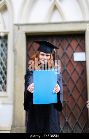 Glücklicher Absolvent. Ich gratulierte den Absolventen von University.graduate Mädchen im Mantel hält in Händen Abschlussdiplom Stockfoto