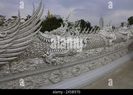 Eine Statue eines Drachen, der das Ende des Drachen vor ihm auf der Brücke zum Weißen Tempel in der Provinz Chiang Rai, Thailand, isst Stockfoto