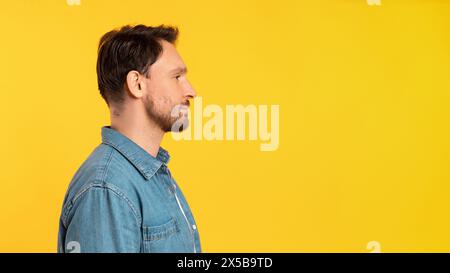 Mann, der vor gelbem Hintergrund steht und den Kopierraum beobachtet Stockfoto