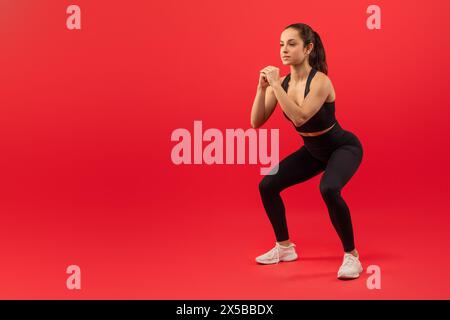 Junge Frau, die eine Squat-Übung vor rotem Hintergrund durchführt Stockfoto