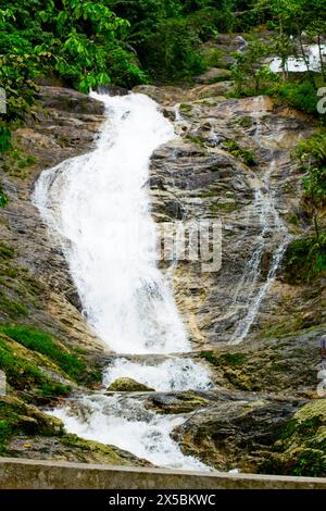 Die ruhige Schönheit eines kleinen Wasserfalls in Malaysia ist ein Touristenziel. Seidenglattes Wasser kaskadiert über Felsen, umgeben von hoch aufragenden Bäumen. Stockfoto