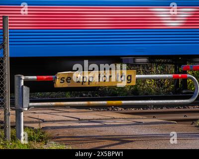 Schwedischer Zug, der an einem Bahnübergang vorbeifährt, mit einem Warnschild mit der Aufschrift „Acht auf Züge“ in schwedischer Sprache - „se upp för tåg“ Stockfoto