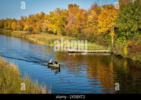 Der wunderschöne Mississippi River in Bemidji, Minnesota, mit einem kleinen Boot mit einem Mann und zwei schwarzen Laborhunden auf dem blauen Wasser und Herbstfarben in t Stockfoto