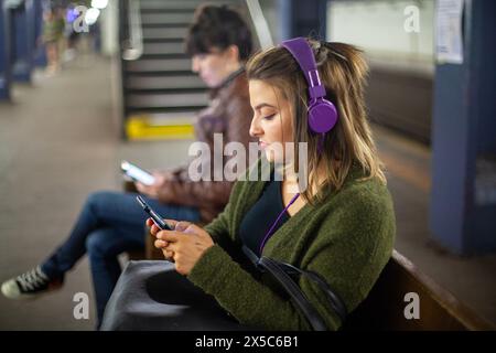 Eine Frau mit Kopfhörern schaut in der U-Bahn in New York City, USA, auf ihr Telefon. Stockfoto