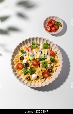 Bunter Nudelsalat mit Farfalle, Kirschtomaten, Oliven, Mozzarella, Brokkoli, und Petersilie auf weißem Hintergrund Stockfoto