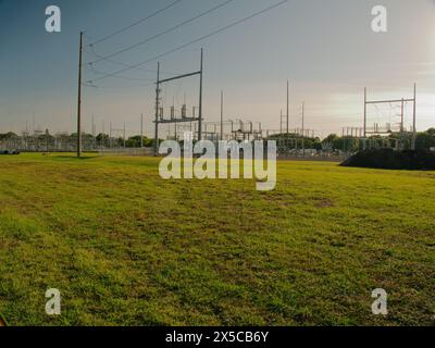 Weite Aussicht bei Sonnenuntergang auf eine elektrische Umspannstation mit Hochspannungsleitungen in St. Petersburg, Florida. Blick auf grünes Gras, blauer Himmel mit großem Metall Stockfoto