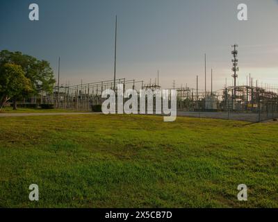 Weite Aussicht bei Sonnenuntergang auf eine elektrische Umspannstation mit Hochspannungsleitungen in St. Petersburg, Florida. Blick auf grünes Gras, blauer Himmel mit großem Metall Stockfoto