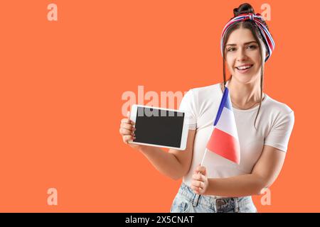 Junge Frau mit Flagge von Frankreich und Tablet-Computer auf orangem Hintergrund Stockfoto