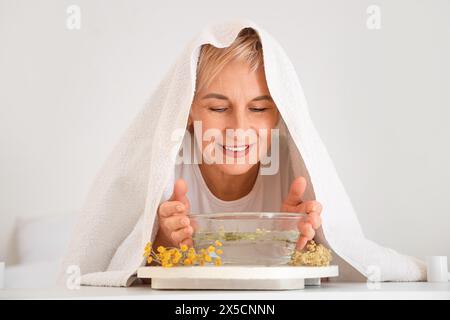 Reife Frau mit Handtuch, die im Schlafzimmer Dampf einatmet Stockfoto