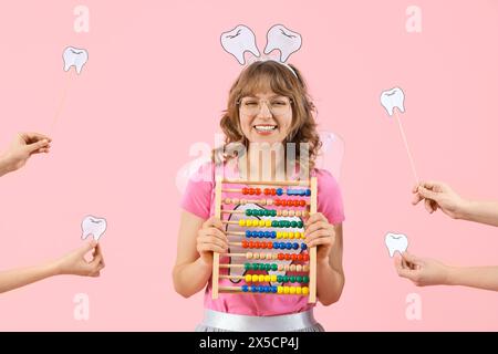 Zahnfee hält Abacus und Hände mit Papierzähnen auf rosa Hintergrund Stockfoto