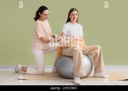 Junge schwangere Frau, die von Doula auf dem Fitball in der Nähe der grünen Wand massiert wird Stockfoto