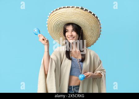 Junge Frau mit Maracas, Sombrero und Poncho auf blauem Hintergrund. Cinco de Mayo-Feier Stockfoto