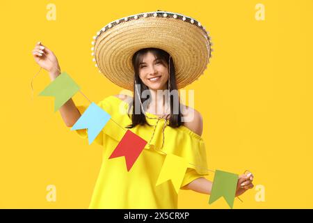Junge Frau im Sombrero, die bunte Fahnen auf gelbem Hintergrund hält. Cinco de Mayo-Feier Stockfoto