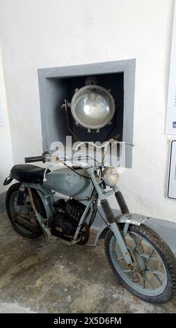 Asinara, Italien. August 2021. Altes Motorrad und ein großer Scheinwerfer am Eingang zum Gefängnismuseum auf dem Hügel der Insel. Stockfoto