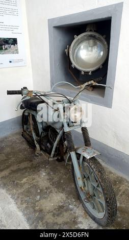 Asinara, Italien. August 2021. Altes Motorrad und ein großer Scheinwerfer am Eingang zum Gefängnismuseum auf dem Hügel der Insel. Stockfoto