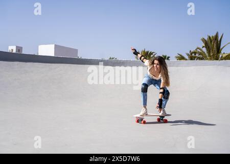 Eine junge Anfängerin, die selbstbewusst die Seite einer Rampe auf einem Skateboard heruntersurft und dabei Geschicklichkeit und Entschlossenheit in Aktion zeigt. Stockfoto