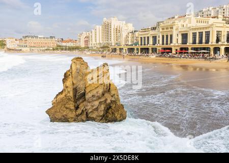 Die schäumenden Wellen stürzen auf den Sandstrand La Grande Plage mit einem gelben Felsen und Gebäude der Stadt im Hintergrund. Biarritz, Frankreich. Stockfoto