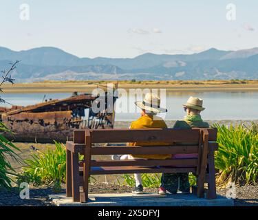 Motueka, Region Tasman, Südinsel, Aotearoa/Neuseeland - 17. März 2024: Älteres Paar mit Strohhüten auf einer Parkbank im Janie Seddon Stockfoto