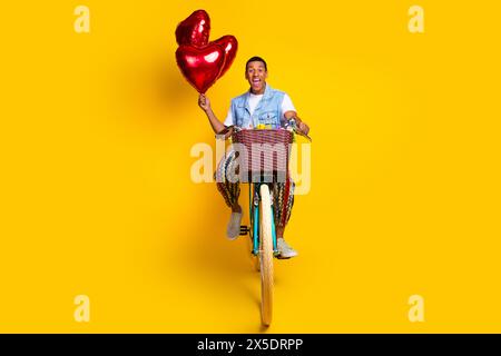 Foto in voller Länge von optimistisch beeindruckt Guy gekleidete Jeans Weste Fahrt auf Fahrradblasen isoliert auf gelbem Hintergrund Stockfoto