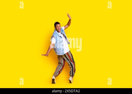 Foto in voller Größe von beeindrucktem exzentrischem Mann gekleidete Jeansweste Hose, die auf Zehenspitzen steht, isoliert auf leuchtendem gelbem Hintergrund Stockfoto