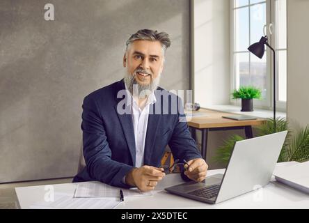 Ein junger Geschäftsmann, der am Schreibtisch im Büro arbeitet und lächelnd in die Kamera schaut. Stockfoto