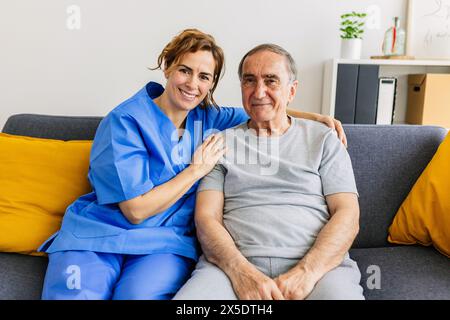 Porträt einer jungen Pflegerin, die mit einem alten Mann auf dem Sofa sitzt. Stockfoto