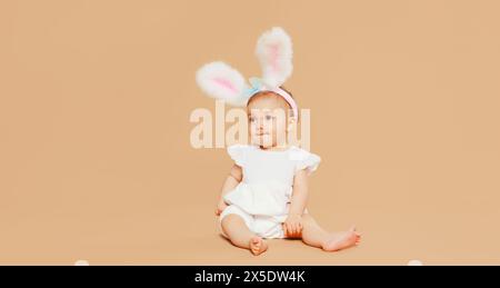 Porträt des süßen Babys mit osterkaninchenohren, die auf braunem Studiohintergrund sitzen Stockfoto