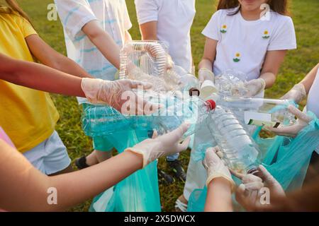 Verschiedene Plastikbehälter befinden sich in den Händen von Kindern, die Müll im Park aufräumen. Stockfoto