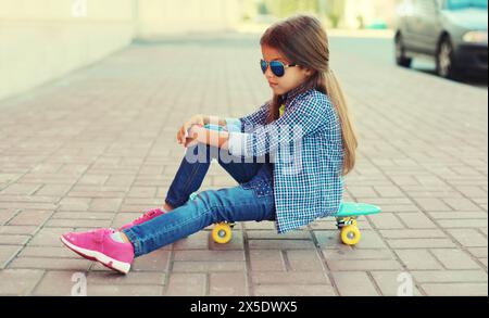 Porträt eines stilvollen kleinen Mädchens, das mit Skateboard auf der Stadtstraße posiert Stockfoto