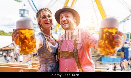 Bayerisches Paar in traditioneller bayerischer Kleidung, das fröhlich mit Bierbecher auf dem oktoberfest oder Duld in deutschland röstet Stockfoto