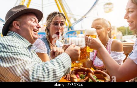 Eine Gruppe von Männern und Frauen in Tracht trinkt Bier und feiert eine Party mit Bierbecher in einem Bierzelt bei Dult oder Oktoberfest Stockfoto
