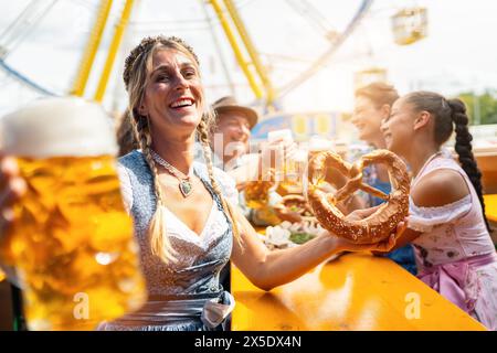 Vier Freunde im Bierzelt bei Dult oder Oktoberfest halten eine riesige Brezel und Bierbecher in der Luft Stockfoto