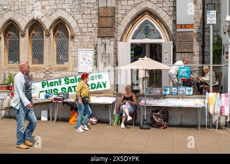 Ein Pflanzenverkauf außerhalb der United Reform Church in The Strand, Dawlish, Devon, England, Großbritannien. Passanten und Damen, die Waren verkaufen. Stockfoto