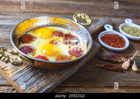 Türkische Wurst und Eier in Kupferpfanne gebraten, Holzhintergrund, Nahaufnahme. Stockfoto