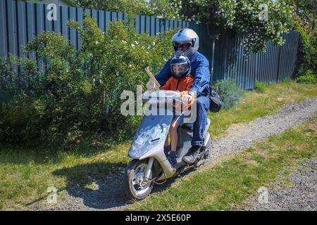 Vater und Sohn fahren am sonnigen Sommernachmittag mit dem Roller durch die Landschaft. Zeit miteinander verbringen. Stockfoto