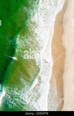 Blick von oben mit Drohne auf die Küste eines Strands mit türkisfarbenem grünem Meer und Surfer mit rotem Surfbrett. Stockfoto