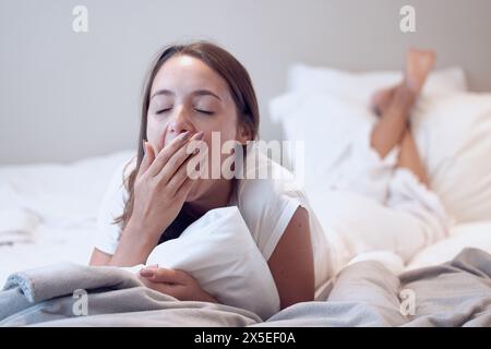 Gähnen, Schläfrigkeit und Frau, die auf dem Bett liegt, für niedrige Energie, erschöpft oder morgens Schlaflosigkeit im Schlafzimmer. Müdigkeit, Student oder weibliche Person decken den Mund für Stockfoto