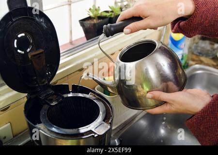 Nahaufnahme einer nicht erkennbaren kaukasischen Frau, die Aluminium-Teekanne hält, Wasser in die Kaffeekanne in der Küche zu Hause gießt. Stockfoto