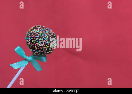Cake Pops in Schokolade mit farbigen Streuseln. Mit einer Schleife verziert. Auf rotem Hintergrund Stockfoto