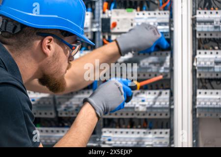 Ein Elektriker arbeitet in einer Schalttafel mit einem elektrischen Anschlusskabel. Stockfoto